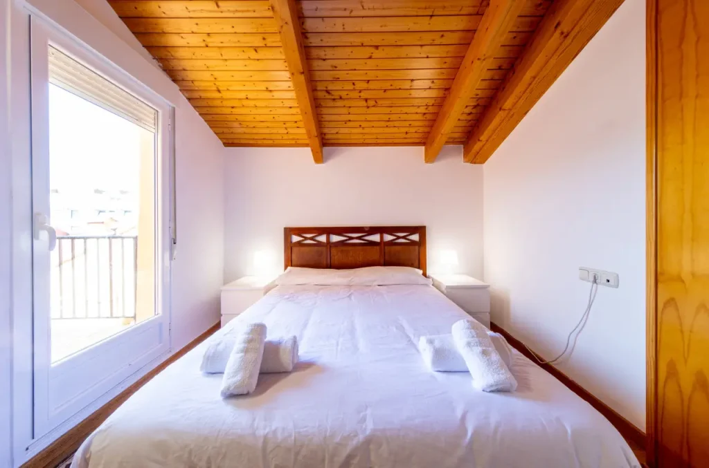 Dormitorio de matrimonio con ventana y ropa de cama blanca